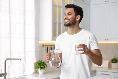 Photo of Happy man with jug and glass of water in kitchen at morning. Space for text