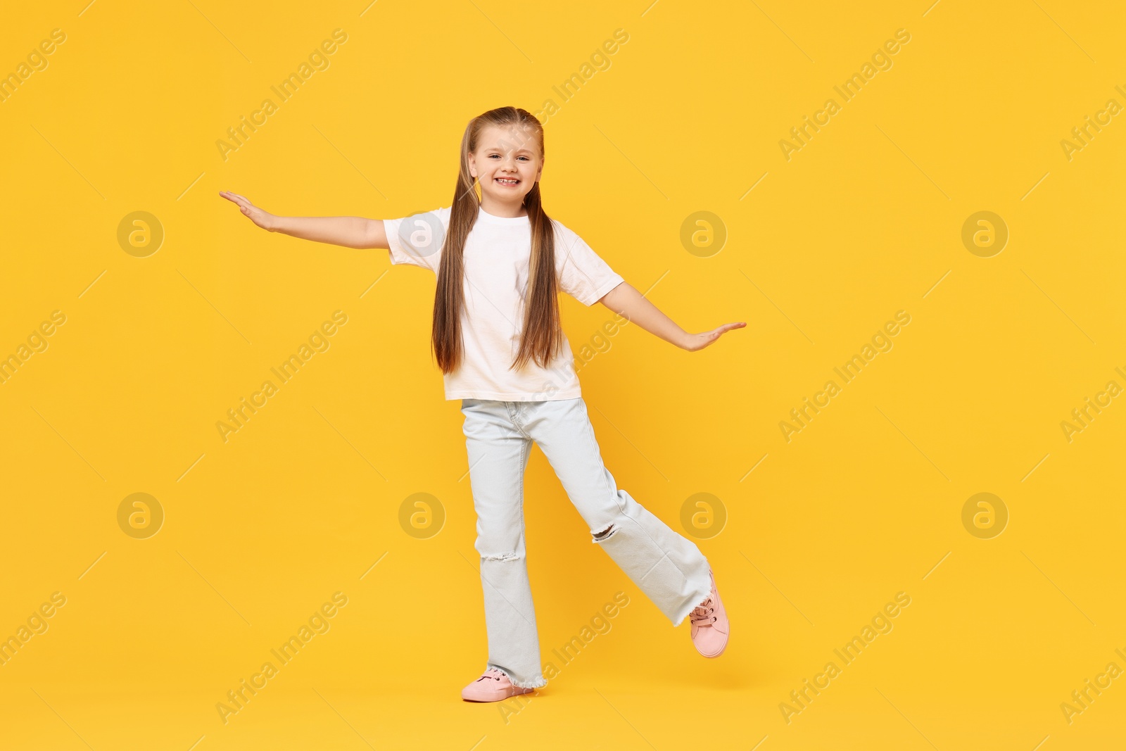Photo of Cute little girl dancing on yellow background