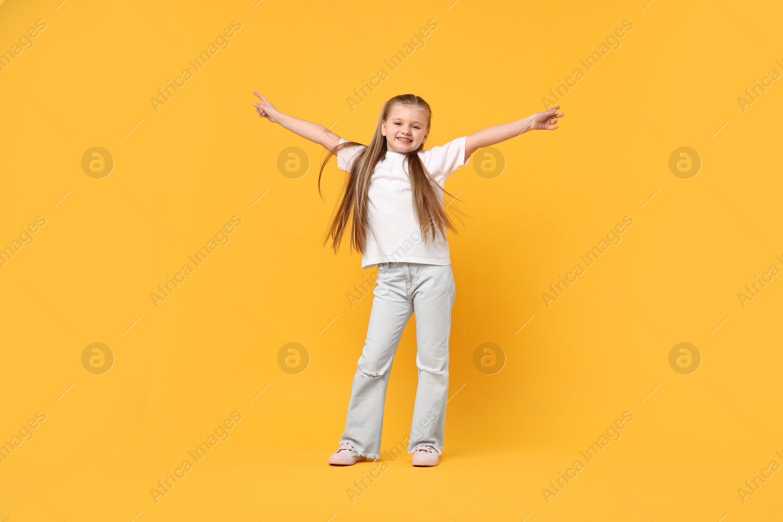 Photo of Cute little girl dancing on yellow background