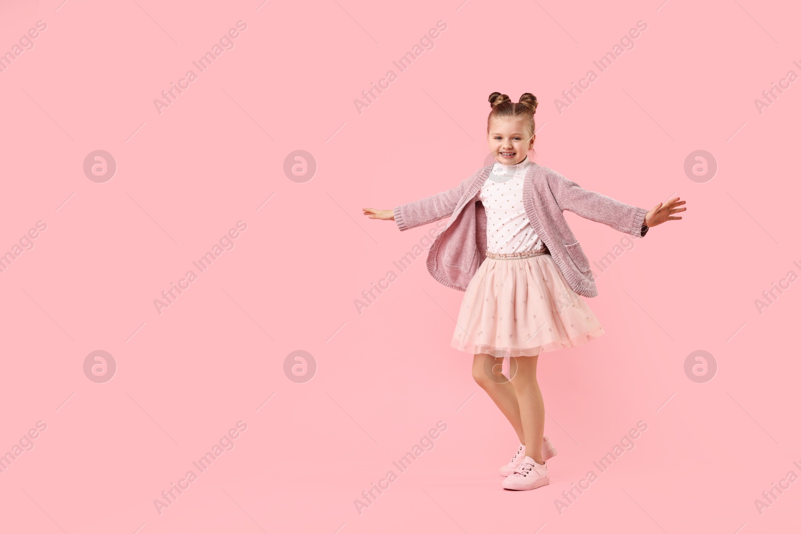 Photo of Cute little girl dancing on pink background, space for text