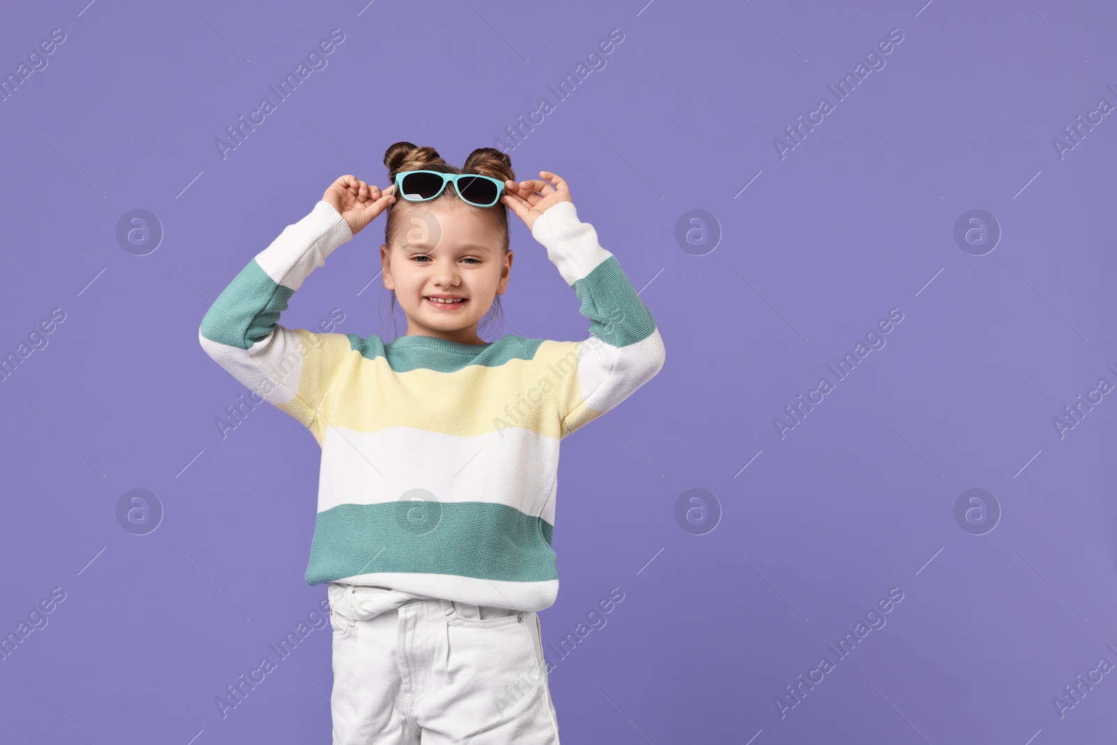 Photo of Cute little girl with sunglasses dancing on violet background, space for text