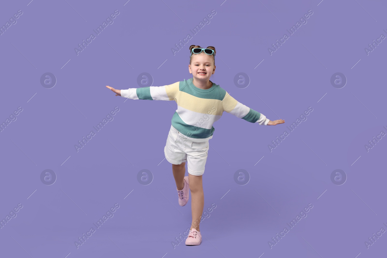 Photo of Cute little girl with sunglasses dancing on violet background