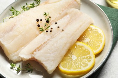 Photo of Plate with raw cod fish, spices, microgreens and lemon on grey table, closeup