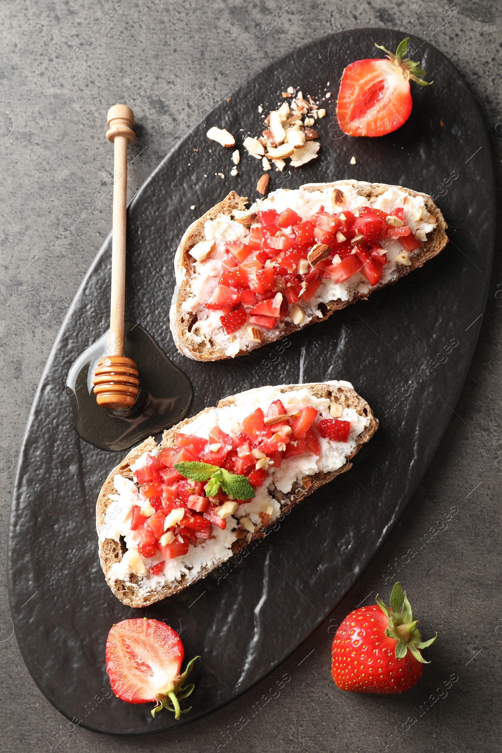 Photo of Bruschettas with ricotta cheese, chopped strawberries, nuts and mint on table, top view