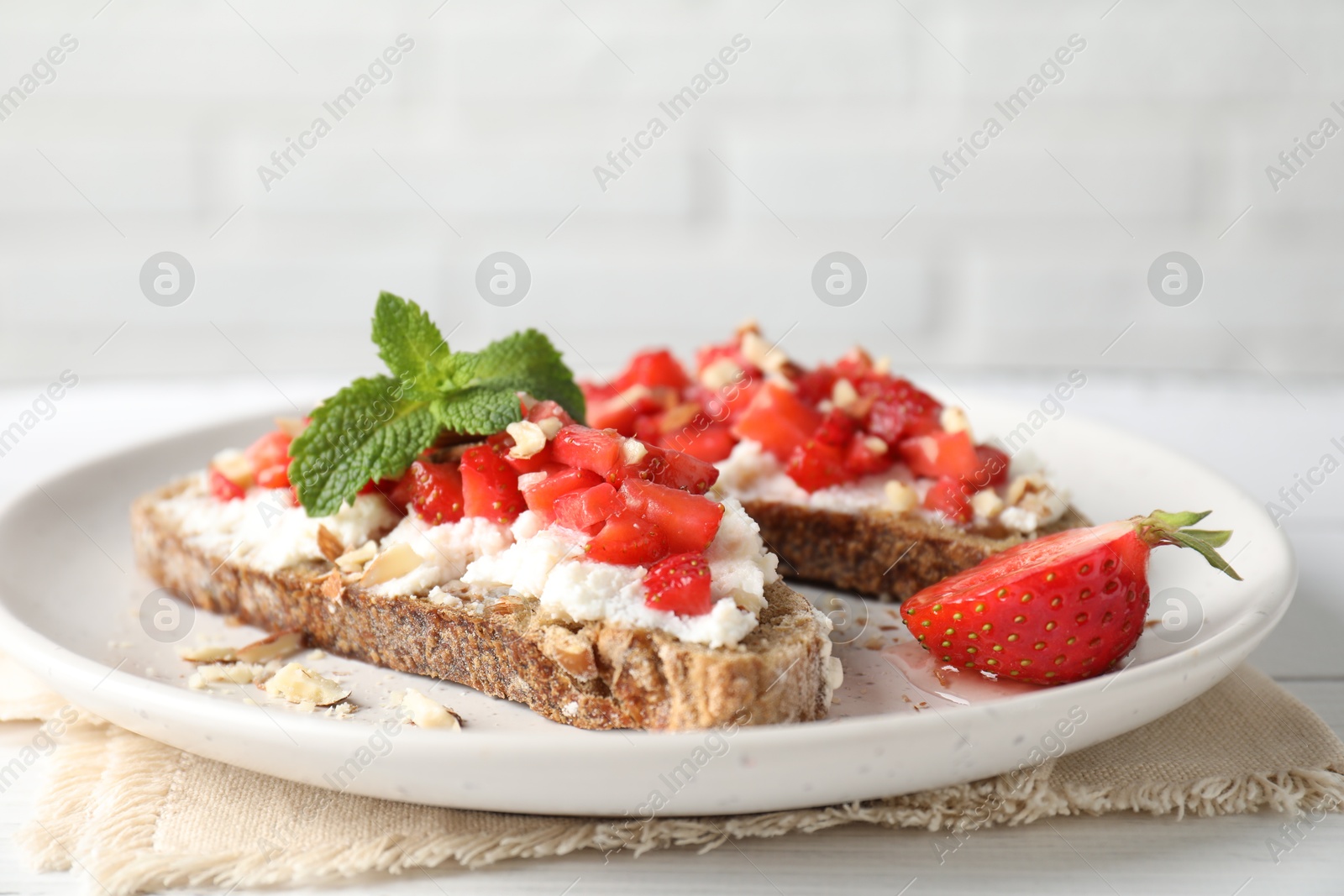 Photo of Bruschettas with ricotta cheese, chopped strawberries and mint on white wooden table, closeup