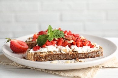 Photo of Bruschettas with ricotta cheese, chopped strawberries and mint on white wooden table, closeup