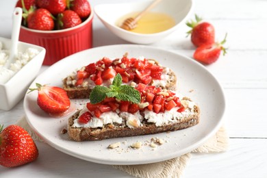 Photo of Bruschettas with ricotta cheese, chopped strawberries and mint on white wooden table, closeup