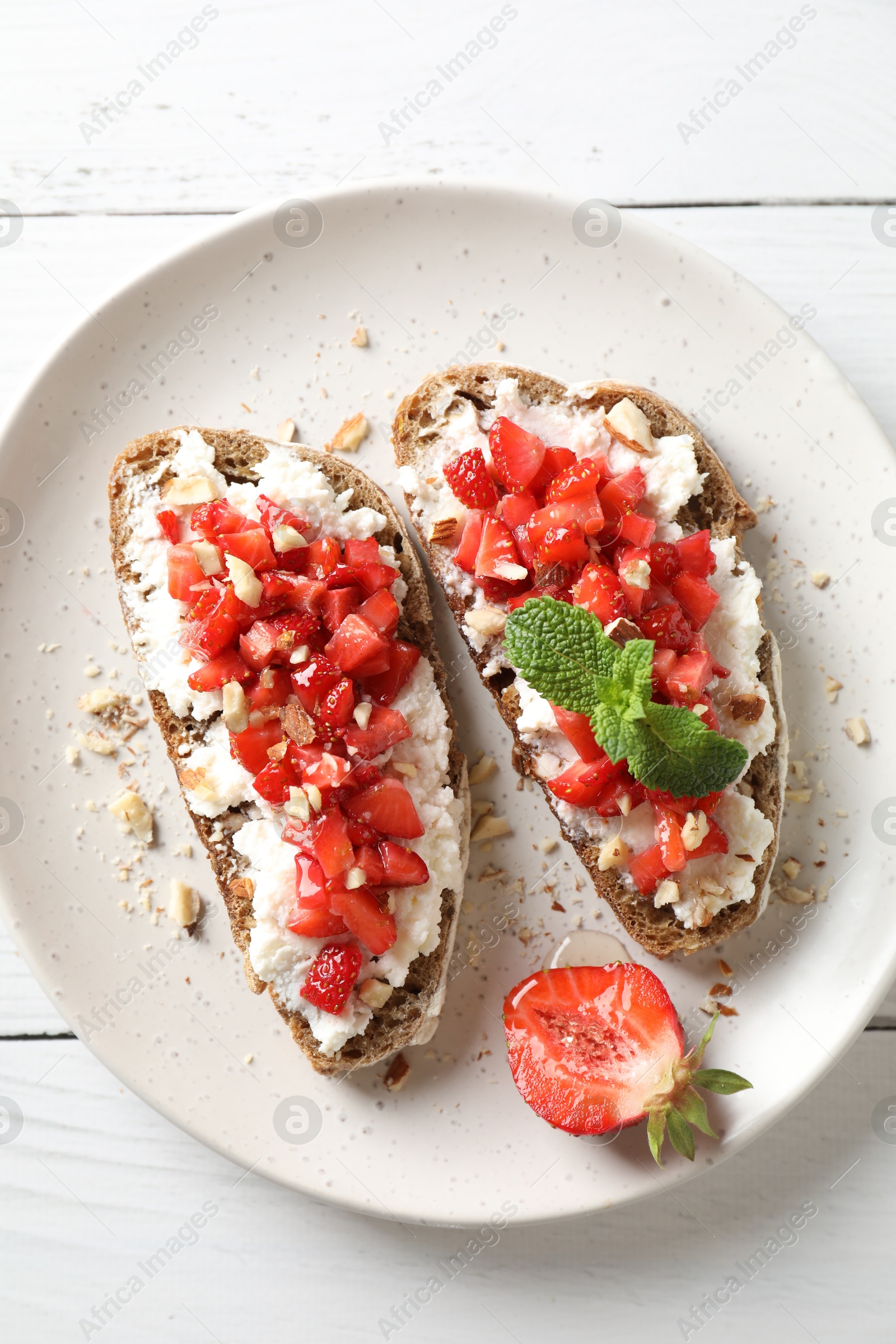 Photo of Bruschettas with ricotta cheese, chopped strawberries and mint on white wooden table, top view
