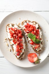 Bruschettas with ricotta cheese, chopped strawberries and mint on white wooden table, top view