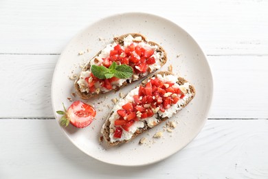 Bruschettas with ricotta cheese, chopped strawberries and mint on white wooden table, top view