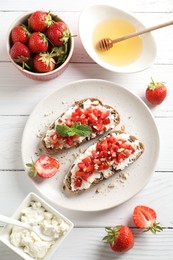 Photo of Bruschettas with ricotta cheese, chopped strawberries and mint on white wooden table, flat lay
