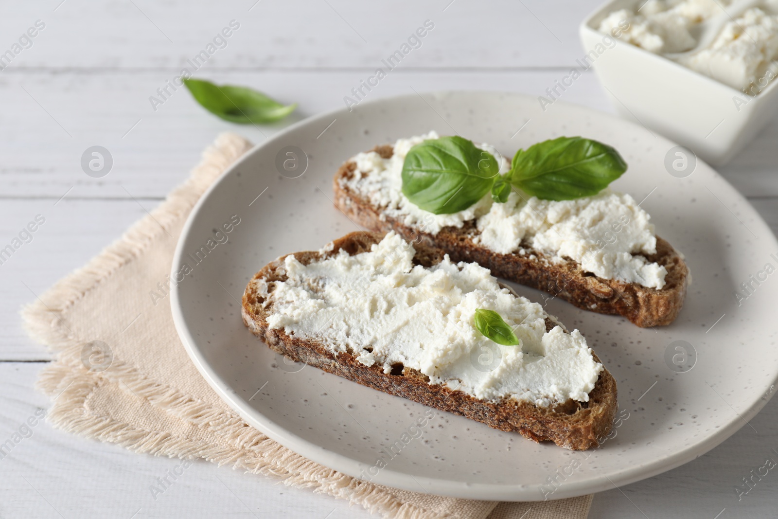 Photo of Bruschettas with ricotta cheese and basil on white wooden table, closeup