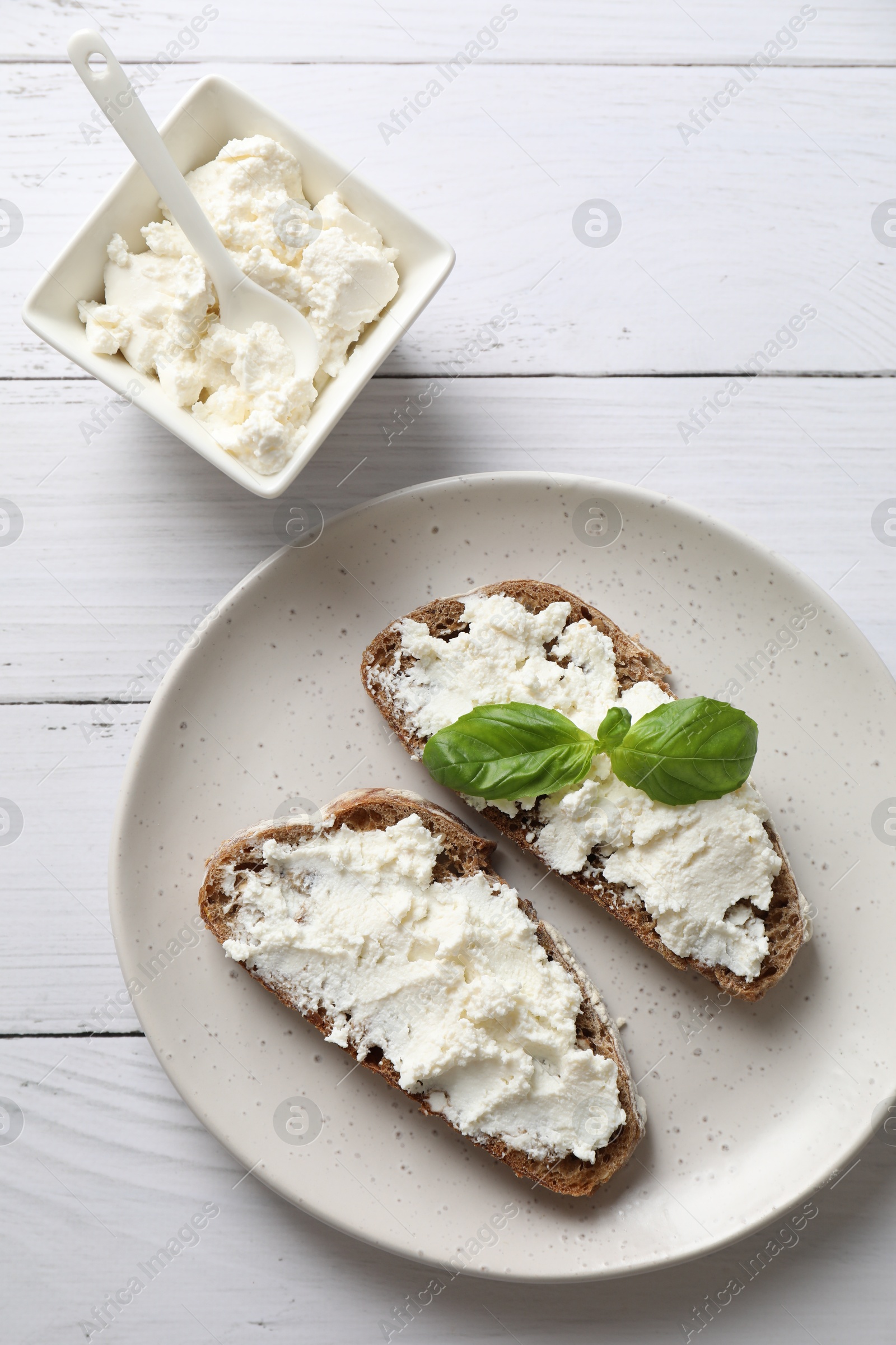 Photo of Bruschettas with ricotta cheese and basil on white wooden table, top view