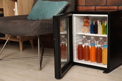 Photo of Mini refrigerator with drinks and snacks indoors