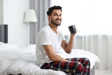 Happy man with cup of coffee on bed at morning