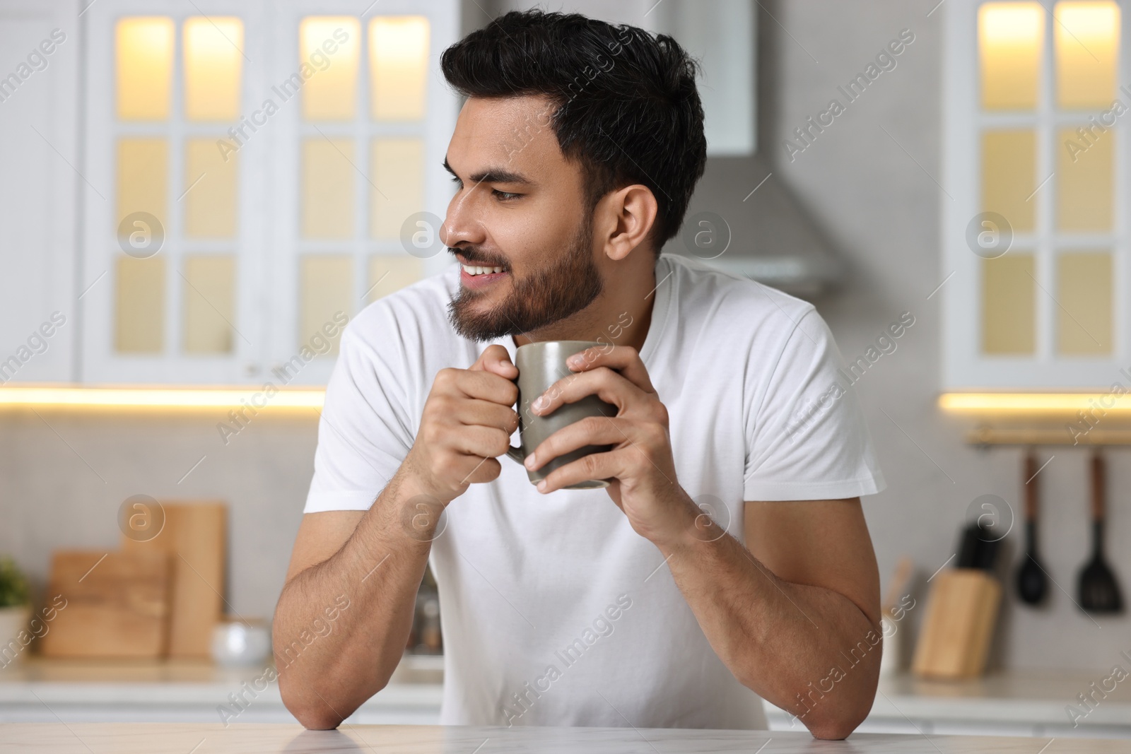 Photo of Morning of happy man with cup of hot drink at table in kitchen