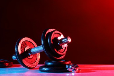 Photo of Barbell and parts of one on table in color lights. Space for text
