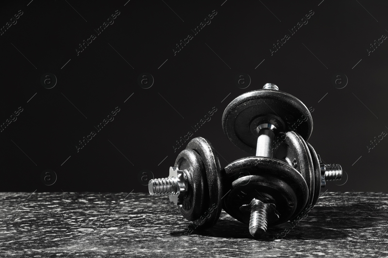 Photo of Two barbells on grey textured table against black background. Space for text