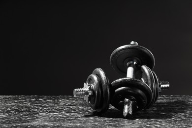Two barbells on grey textured table against black background. Space for text