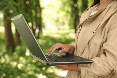 Forester with laptop examining plants in forest, closeup