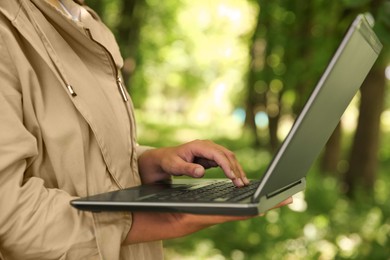 Forester with laptop examining plants in forest, closeup