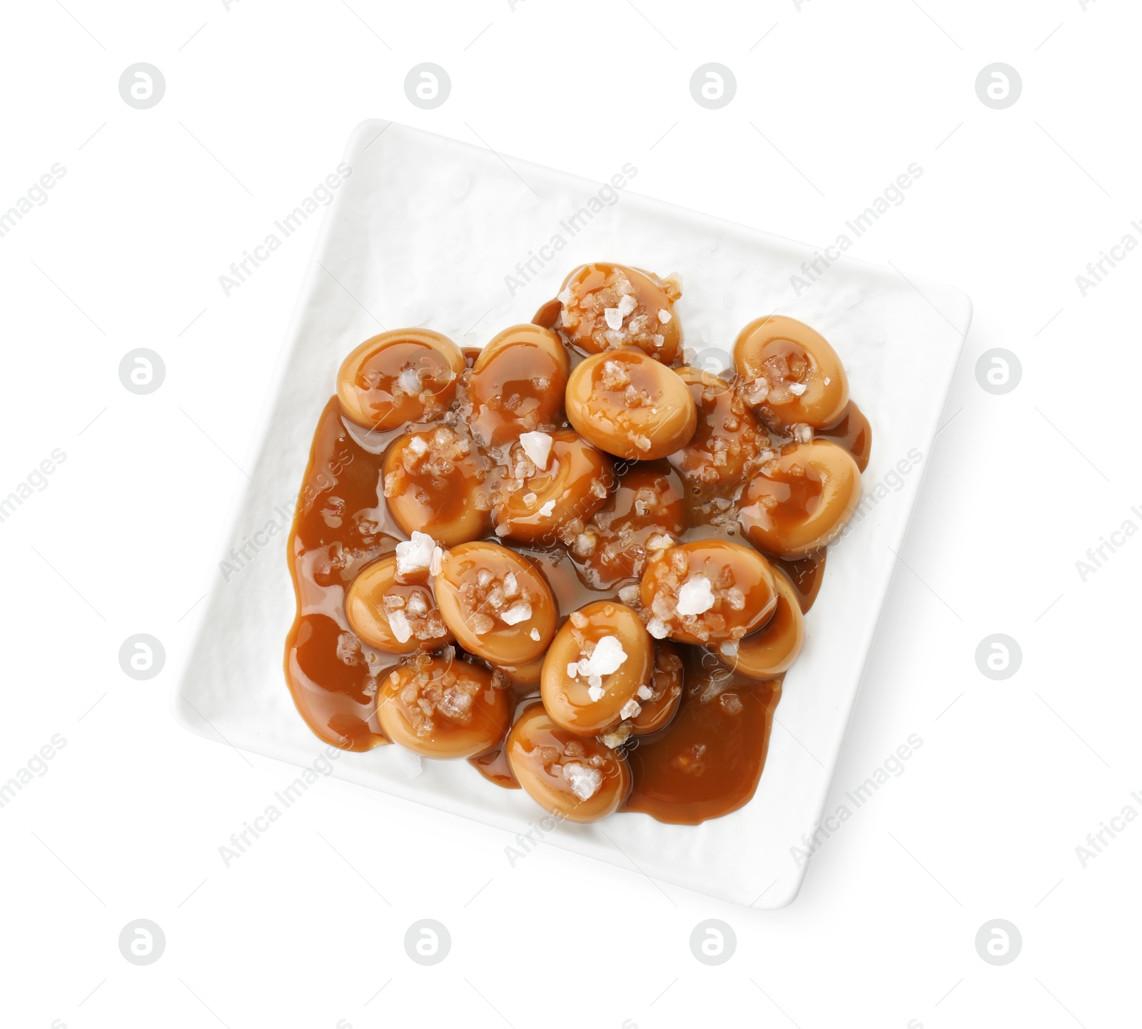 Photo of Plate with tasty candies, caramel sauce and salt isolated on white, top view
