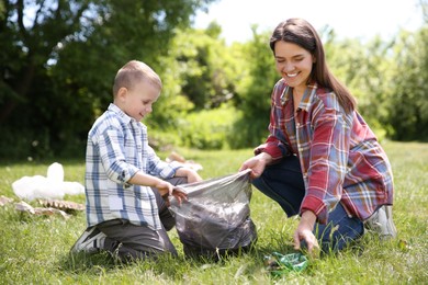 Mother and her son with plastic bag collecting garbage in park