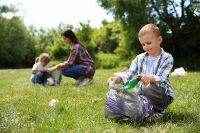 Mother and her children with plastic bags collecting garbage in park