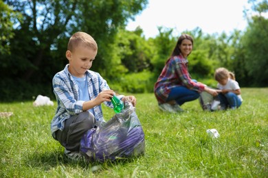 Photo of Mother and her children with plastic bags collecting garbage in park