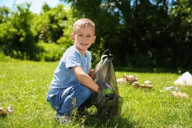 Photo of Little boy with plastic bag collecting garbage in park
