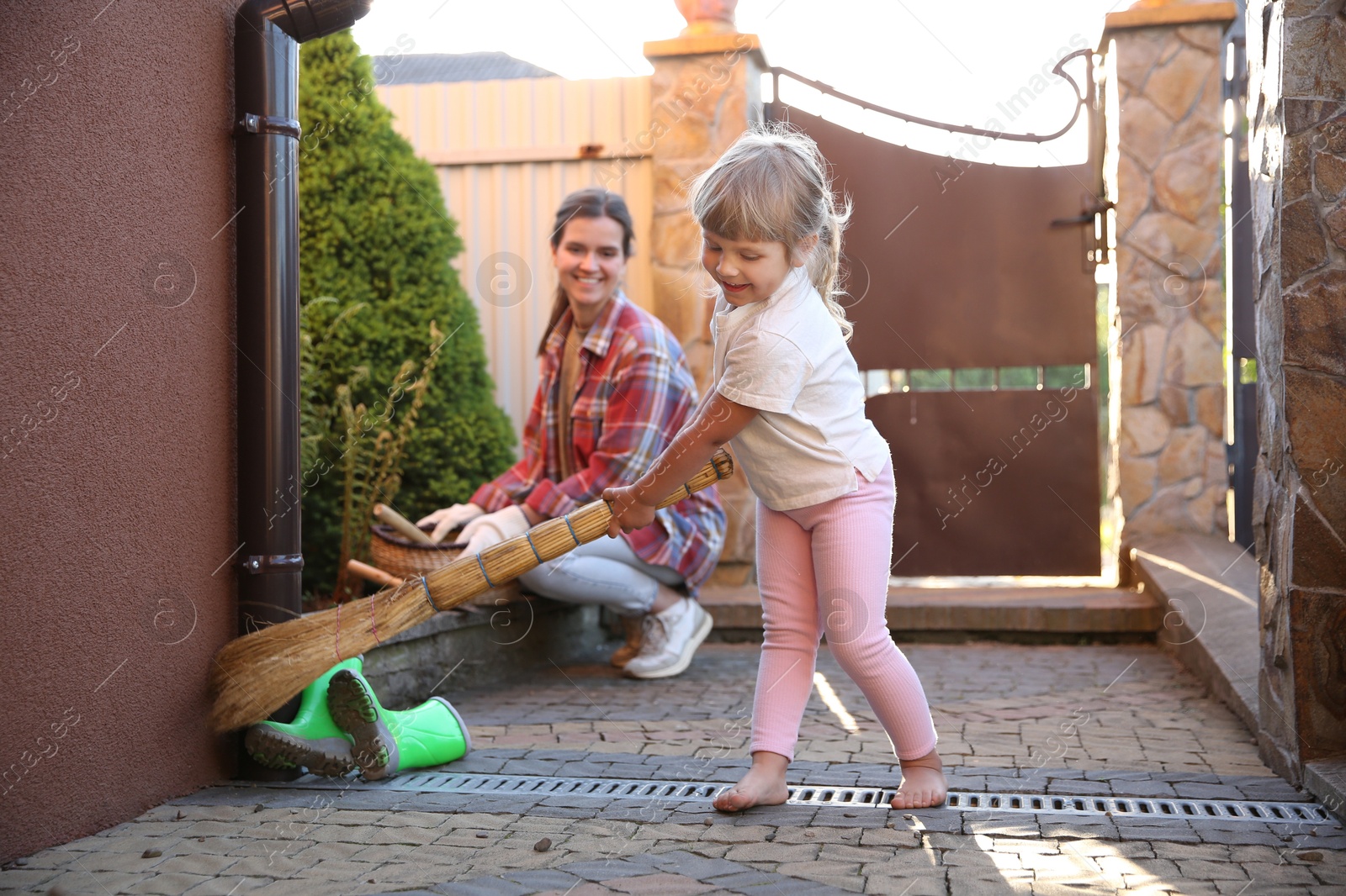 Photo of Mother and her cute daughter cleaning near house together on spring day