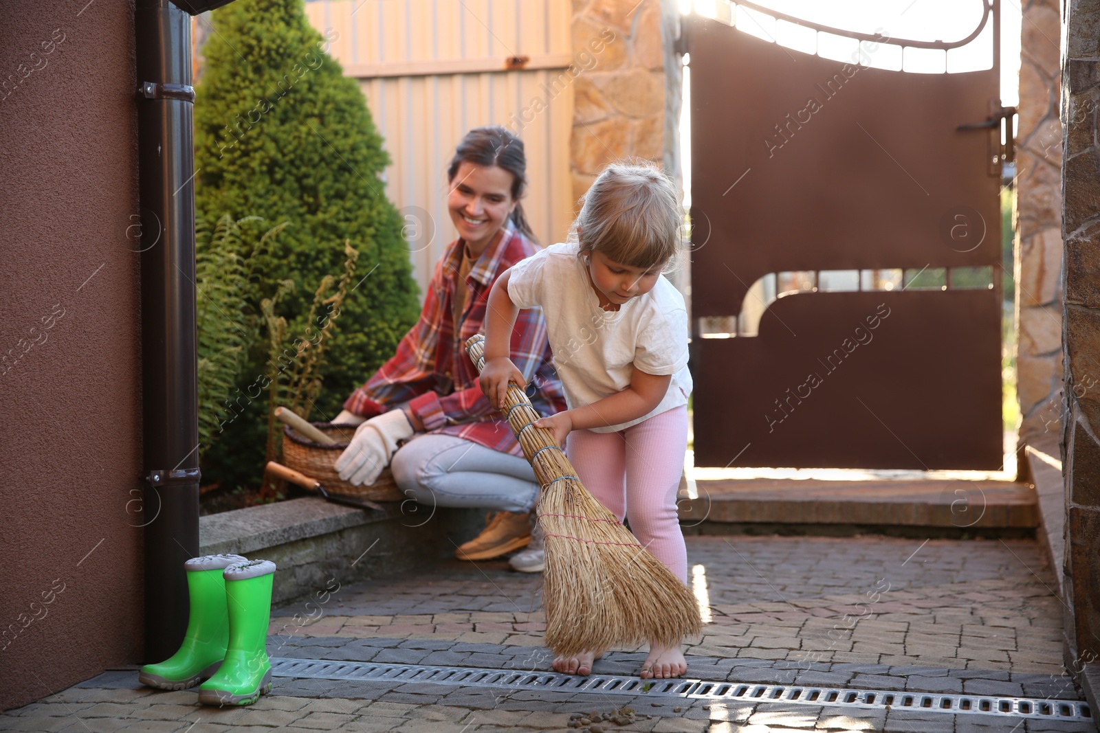 Photo of Mother and her cute daughter cleaning near house together on spring day