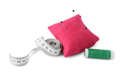 Photo of Pink pincushion with sewing pins, measuring tape and spool of thread isolated on white