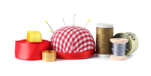 Photo of Pincushion, sewing pins, thimble, spools of threads, measuring tape and ribbons isolated on white