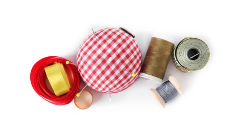 Photo of Pincushion, sewing pins, thimble, spools of threads, measuring tape and ribbons isolated on white, top view