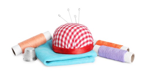 Pincushion, sewing needles, spools of threads, cloth and thimble isolated on white