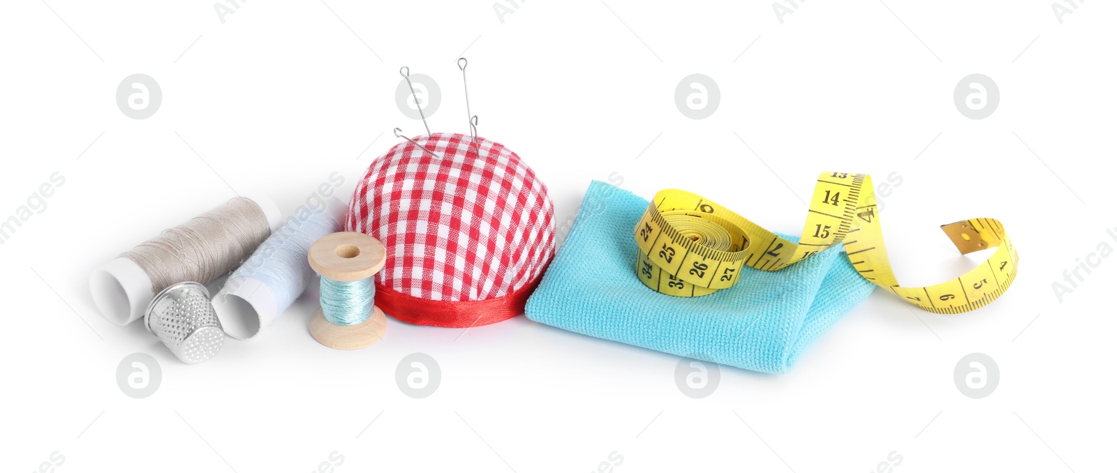 Photo of Pincushion, sewing needles, spools of threads, cloth, measuring tape and thimble isolated on white