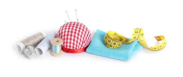 Pincushion, sewing needles, spools of threads, cloth, measuring tape and thimble isolated on white