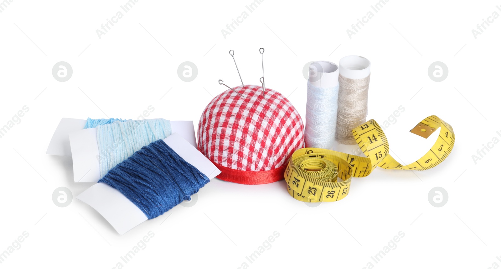 Photo of Pincushion, sewing needles, spools of threads and measuring tape isolated on white