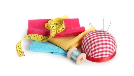 Pincushion, sewing needles, pieces of fabrics, spool of thread and measuring tape isolated on white