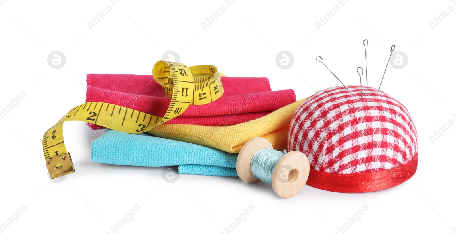 Photo of Pincushion, sewing needles, pieces of fabrics, spool of thread and measuring tape isolated on white