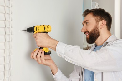 Photo of Smiling man drilling white wall at home