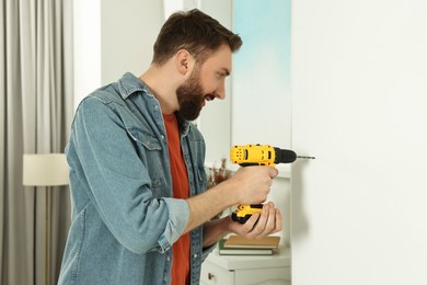 Smiling man drilling white wall at home