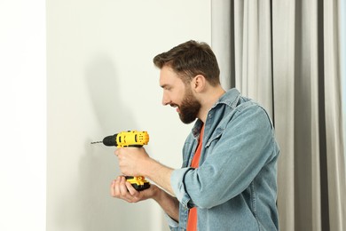 Smiling man drilling white wall at home