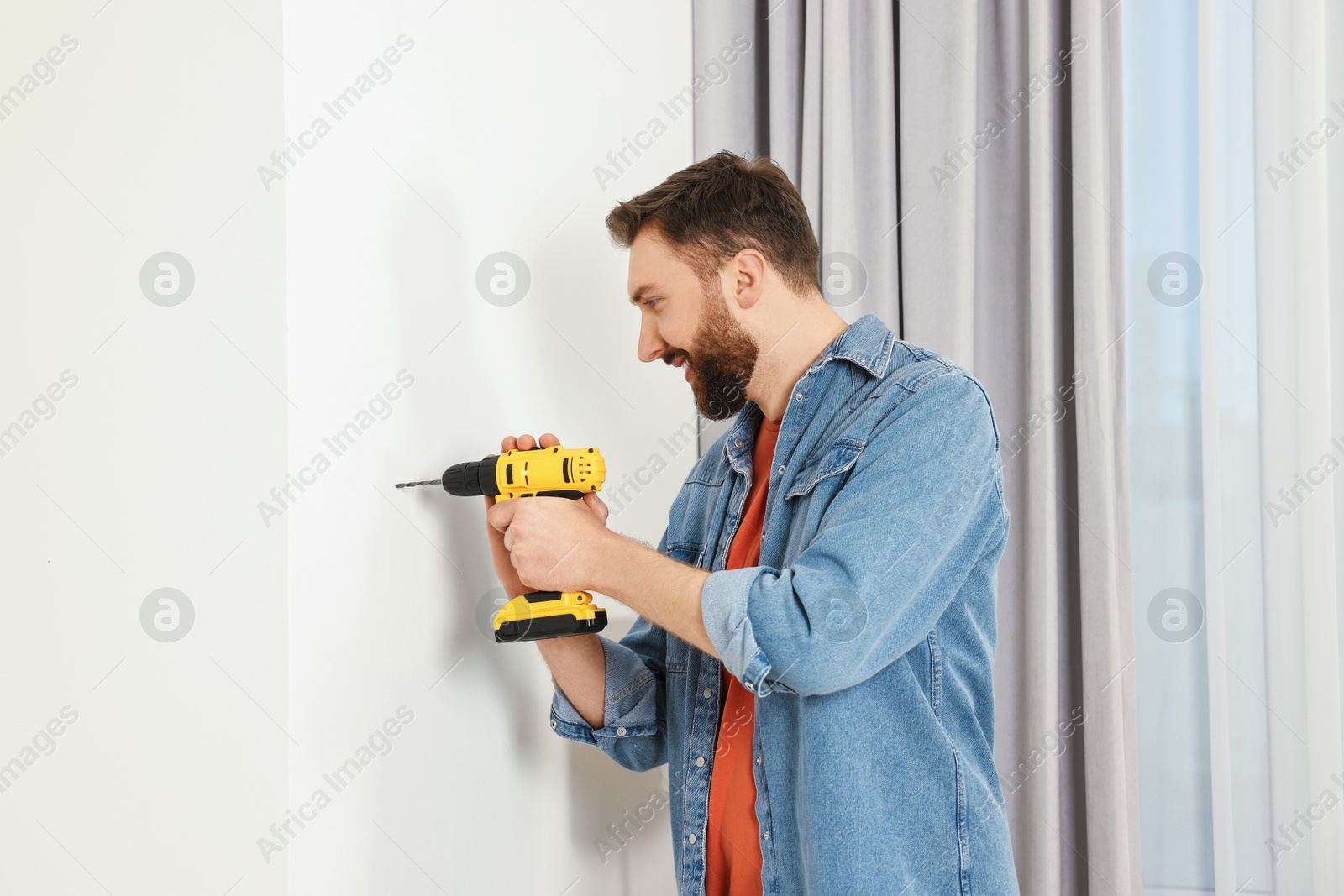 Photo of Smiling man drilling white wall at home