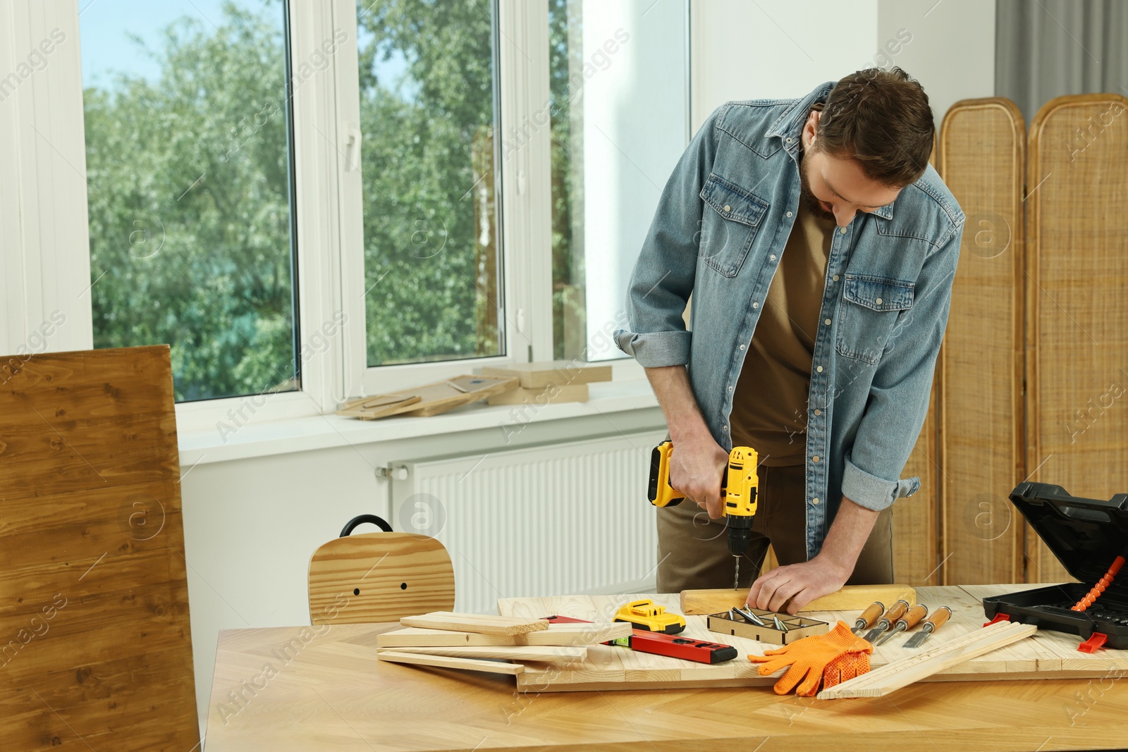 Photo of Craftsman working with drill at wooden table in workshop