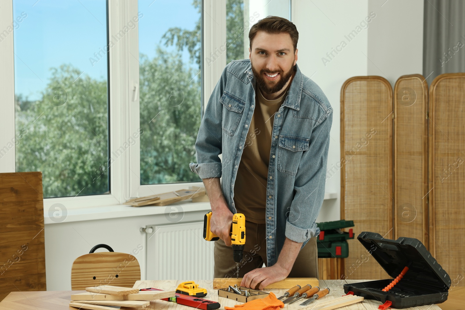 Photo of Portrait of smiling craftsman with drill at table in workshop