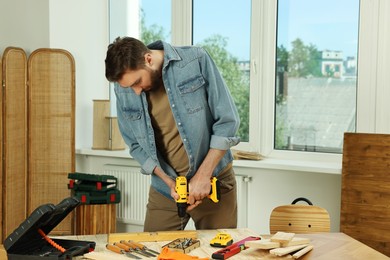 Photo of Craftsman working with drill at wooden table in workshop