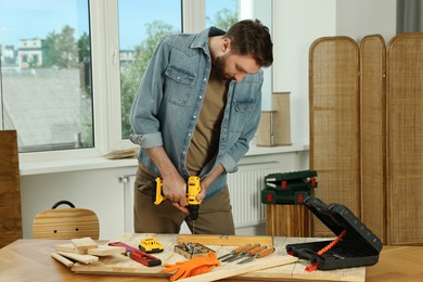 Photo of Craftsman working with drill at wooden table in workshop