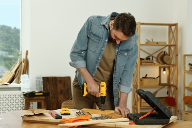 Photo of Craftsman working with drill at wooden table in workshop